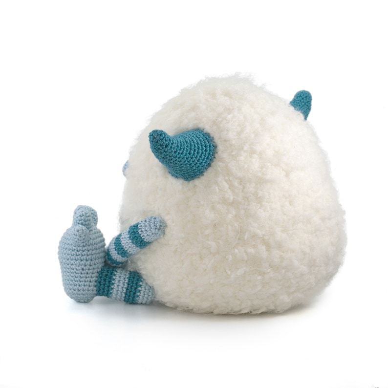 May include: A white crocheted plush toy with blue and white striped legs and blue horns. The toy is sitting on a white background.