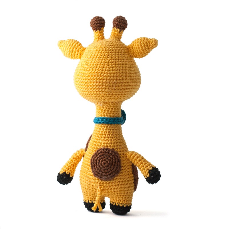 May include: A crocheted giraffe toy with brown spots and a blue collar. The giraffe is standing on a white background.