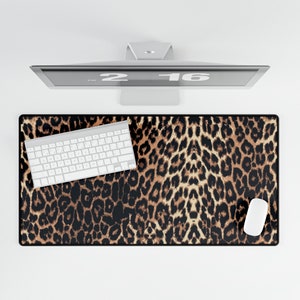 Peut inclure: Un tapis de bureau à imprimé léopard avec un clavier blanc et une souris blanche. Le tapis est brun et noir avec un motif léopard.