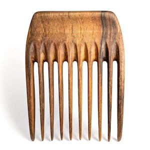 Puede incluir: Un peine de madera con un patrón de veta de madera marrón y negro. El peine tiene nueve dientes y una parte superior redondeada.