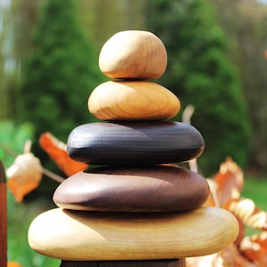 May include: A stack of five wooden discs in various shades of brown, with the top disc being the lightest and the bottom disc being the darkest. The discs are stacked in a pyramid shape, with the top disc being the smallest and the bottom disc being the largest.
