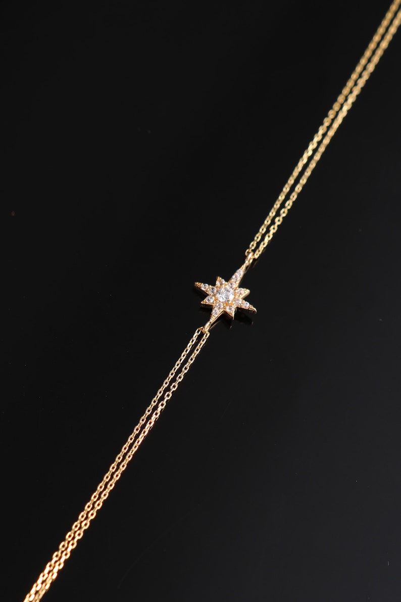 May include: A gold chain bracelet with a star-shaped charm set with clear cubic zirconia stones.