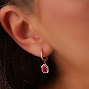 May include: Gold hoop earrings with a dangling red gemstone surrounded by smaller clear gemstones.