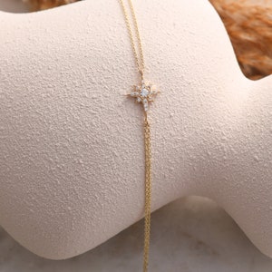 May include: A delicate gold chain necklace with a star-shaped pendant adorned with sparkling white stones.