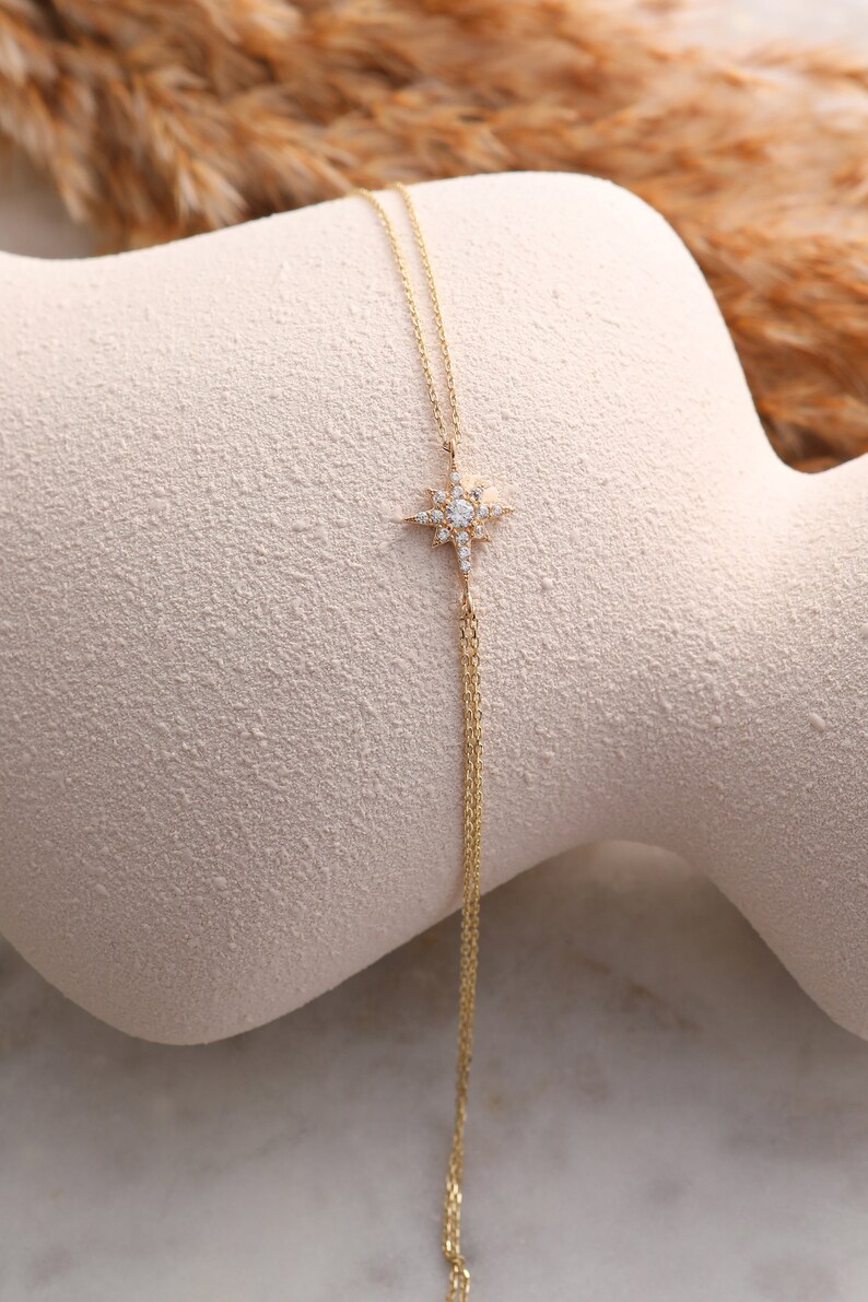 May include: A delicate gold chain necklace with a star-shaped pendant adorned with sparkling white stones.