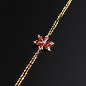 May include: A gold chain bracelet with a red and white flower charm. The flower has a five-petal design with clear stones in the center of each petal.