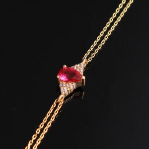 May include: A gold chain necklace with a red gemstone pendant surrounded by smaller clear gemstones.