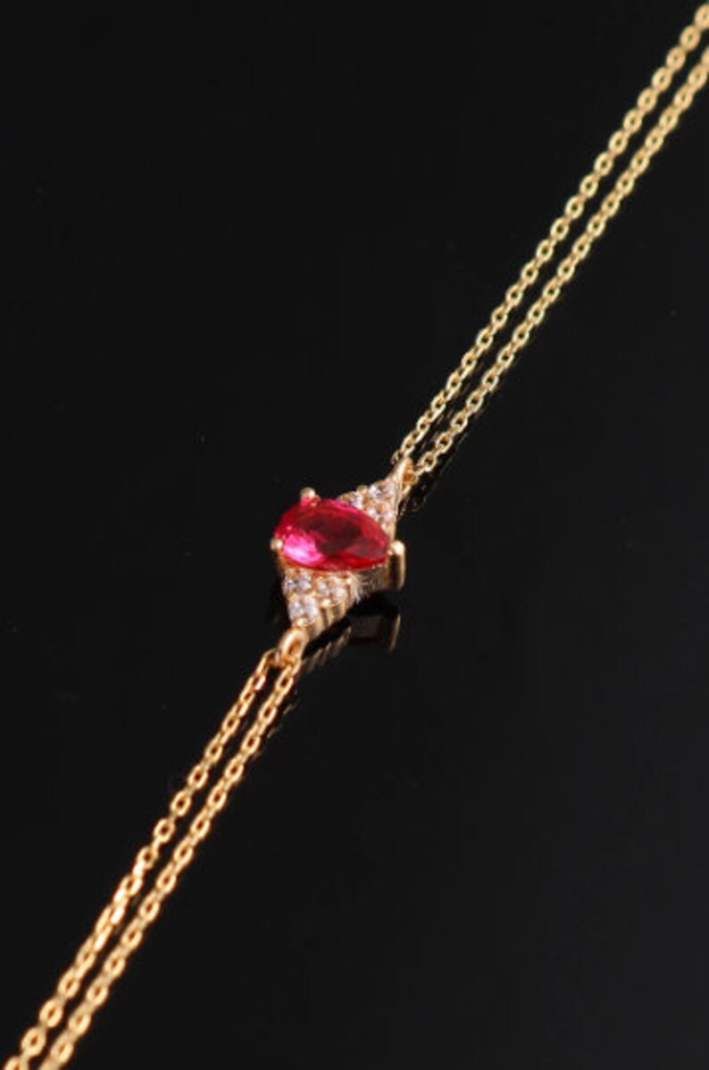 May include: A gold chain necklace with a red gemstone pendant surrounded by smaller clear gemstones.