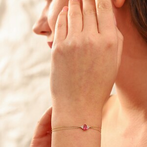 May include: A delicate gold chain bracelet with a pear-shaped pink gemstone and two smaller white gemstones.