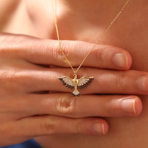 May include: A gold necklace featuring a dainty dove pendant set with black and white cubic zirconia stones.