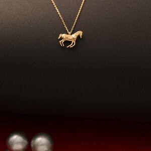 May include: A gold chain necklace with a horse pendant. The necklace is on a black background.