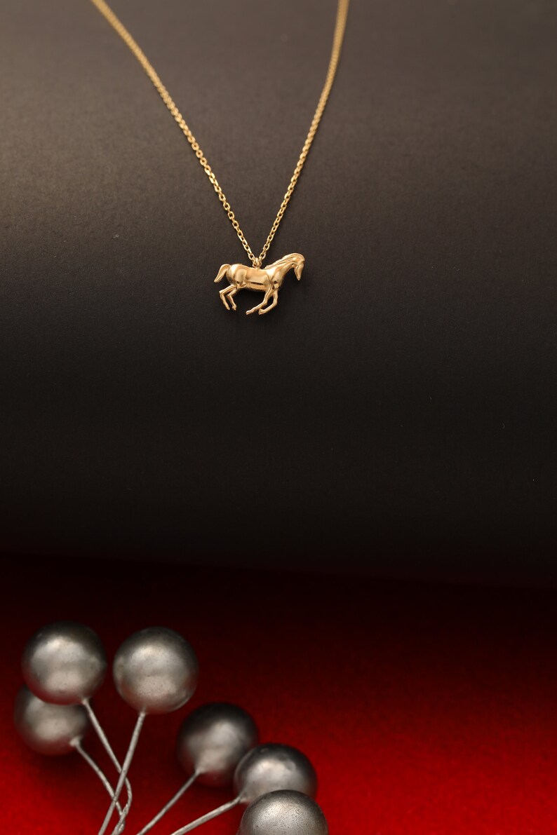 May include: A gold chain necklace with a horse pendant. The necklace is on a black background.