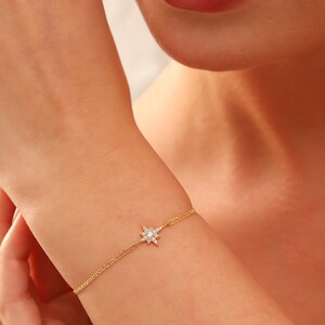 May include: A gold chain bracelet with a small, sparkling star charm. The star is made of clear crystals and is set in a gold frame.