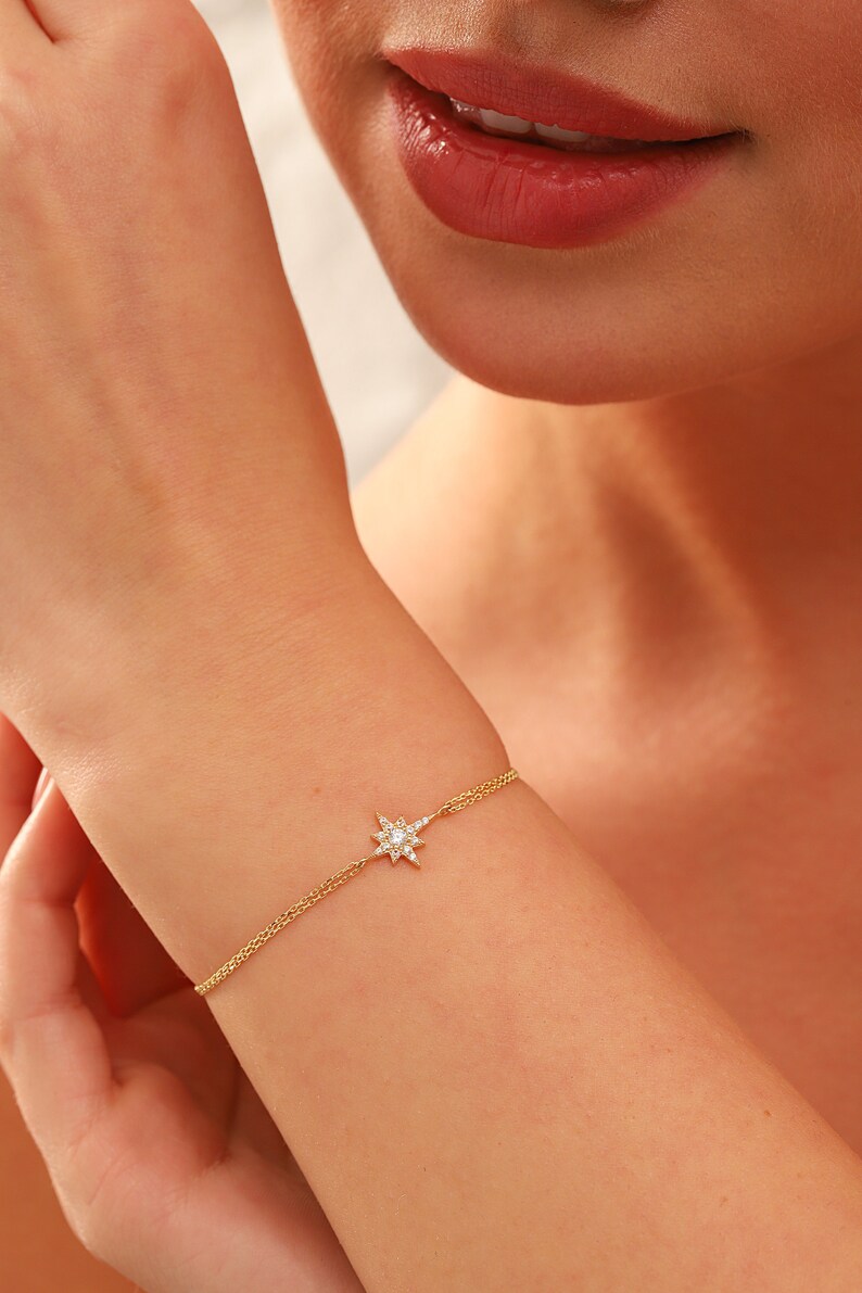 May include: A gold chain bracelet with a small, sparkling star charm. The star is made of clear crystals and is set in a gold frame.