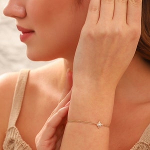 May include: A delicate gold chain bracelet with a small, sparkling star charm. The bracelet is shown on a person's wrist.