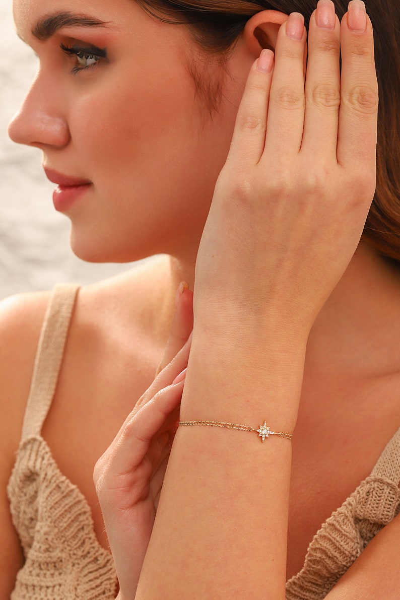 May include: A delicate gold chain bracelet with a small, sparkling star charm. The bracelet is shown on a person's wrist.
