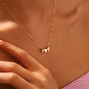Puede incluir: Un collar de oro con una cadena y un colgante hecho de cuatro pequeños cubos de oro conectados.