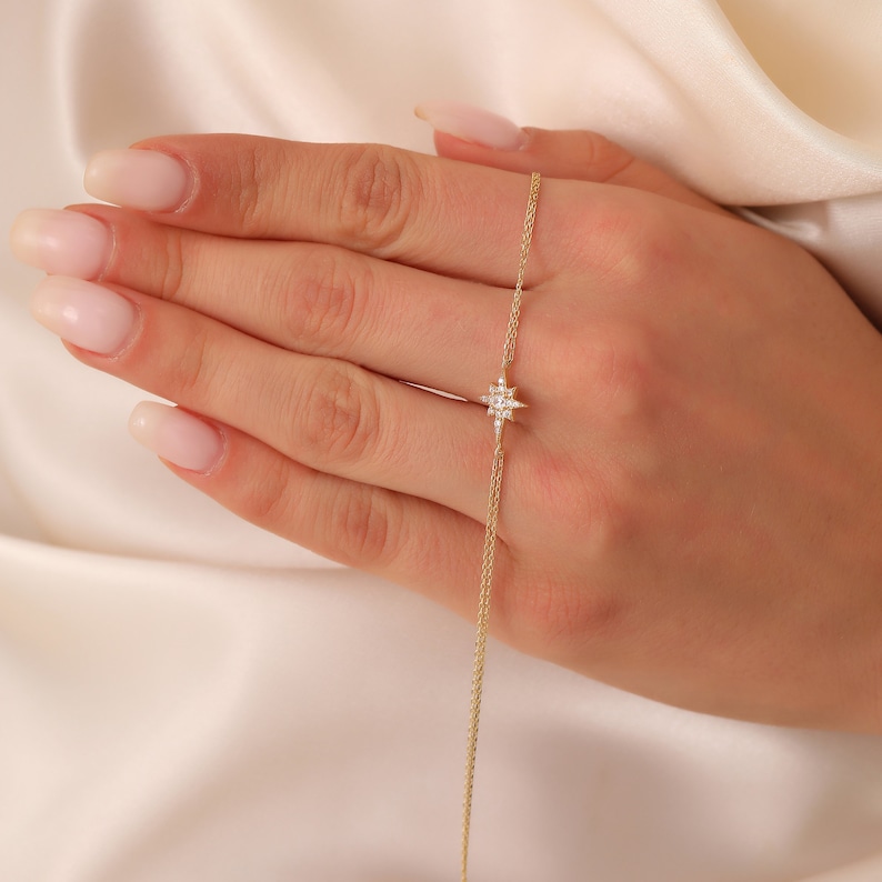 May include: A delicate gold chain necklace with a small, sparkling star pendant. The star is made of clear diamonds and has a pointed design.
