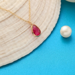 May include: A gold chain necklace with a teardrop-shaped pendant featuring a red gemstone.