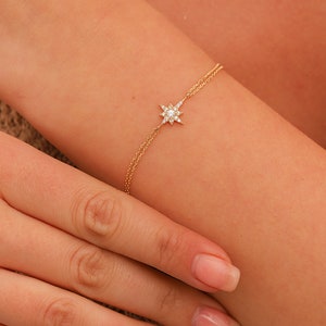 May include: A delicate gold chain bracelet with a small, sparkling star charm. The star is made of diamonds and has a pointed design.