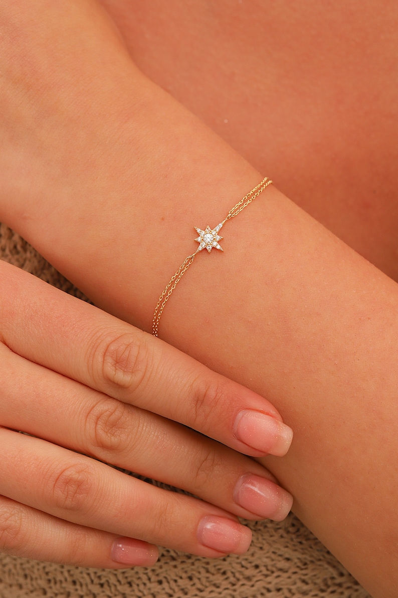 May include: A delicate gold chain bracelet with a small, sparkling star charm. The star is made of diamonds and has a pointed design.