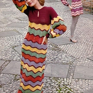 Puede incluir: Un vestido de ganchillo de manga larga con un corpiño rojo oscuro con escote de cerradura y un patrón de chevrón multicolor en amarillo, verde, naranja y lavanda. La prenda tiene mangas amplias y fruncidas y una silueta larga y ajustada.