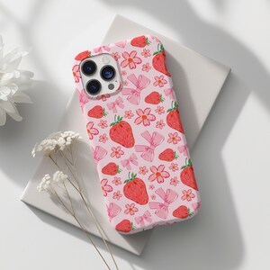 K&ouml;nnte beinhalten: Eine rosa Handyh&uuml;lle mit einem Muster aus Erdbeeren, Blumen und Schleifen. Die H&uuml;lle ist f&uuml;r ein iPhone konzipiert.