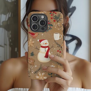 May include: A phone case with a festive winter design. The case features a snowman wearing a red scarf and hat, along with gingerbread cookies, a red bird, and sprigs of berries. The background is a light brown color.