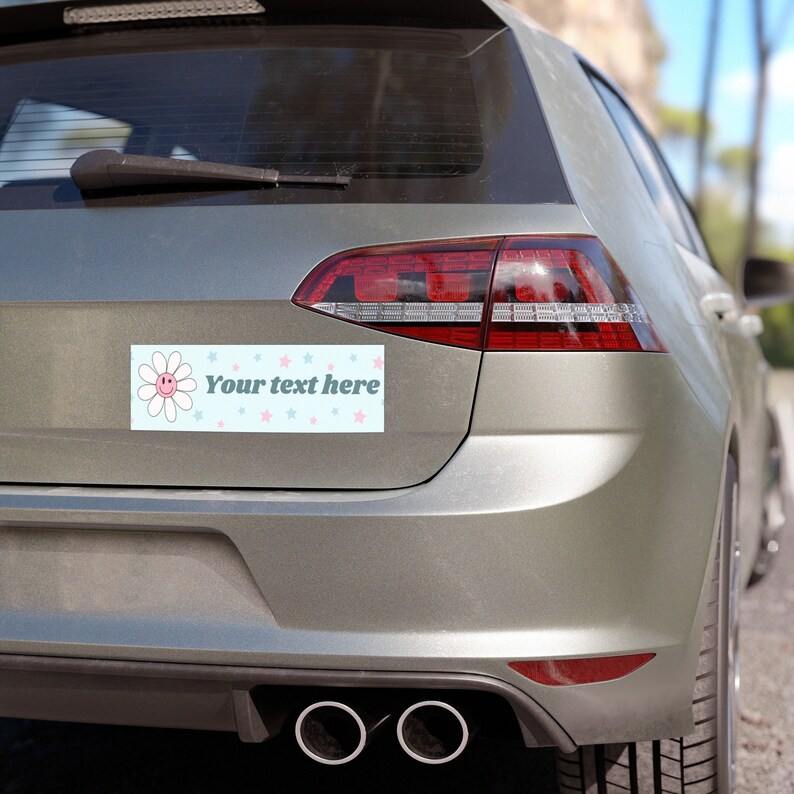 May include: A light blue bumper sticker with a pink daisy and stars. The sticker says "Your text here".