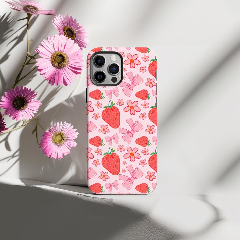 K&ouml;nnte beinhalten: Eine rosa Handyh&uuml;lle mit einem Muster aus Erdbeeren, Blumen und Schleifen. Die H&uuml;lle ist f&uuml;r ein iPhone konzipiert.