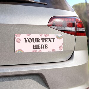 May include: A pink and white car magnet with a rainbow and flowers. The text "YOUR TEXT HERE" is printed in brown on the magnet.