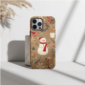May include: A brown phone case featuring a winter-themed design. The case has a repeating pattern of a snowman wearing a red scarf and hat, snowflakes, birds, and sprigs of holly. Other elements include a mug and gingerbread cookies.