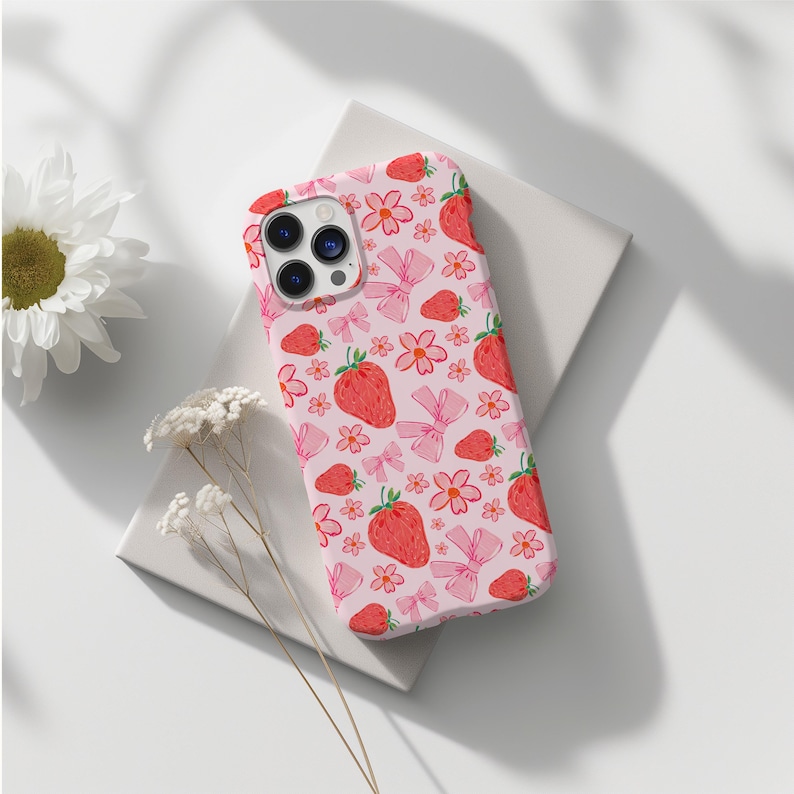 K&ouml;nnte beinhalten: Eine rosa Handyh&uuml;lle mit einem Muster aus Erdbeeren, Blumen und Schleifen. Die H&uuml;lle ist f&uuml;r ein iPhone konzipiert.