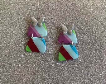 May include: A pair of dangle earrings with a butterfly charm and striped geometric shapes in shades of blue, green, red, and purple.
