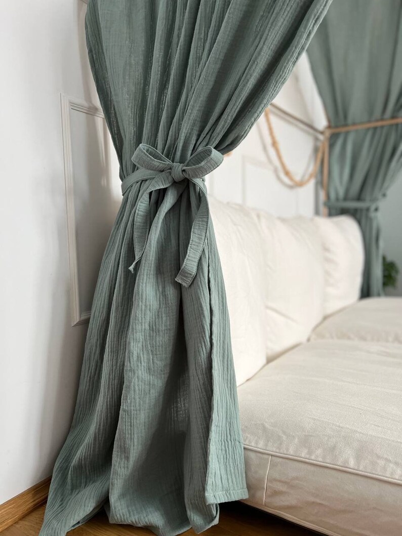 Pu&ograve; includere: Una tenda in cotone verde salvia con un fiocco annodato in cima, appesa davanti a un divano bianco.