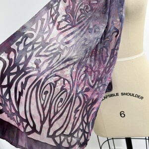 May include: A purple and white silk scarf with a floral pattern. The scarf is draped over a dress form.