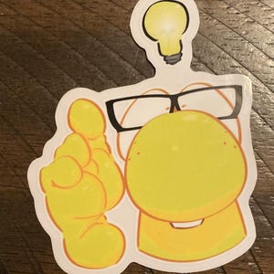 May include: A die-cut sticker featuring a yellow, rounded character wearing black-rimmed glasses. The character has one hand raised with an index finger pointing upward, and a yellow lightbulb icon is positioned directly above its head.