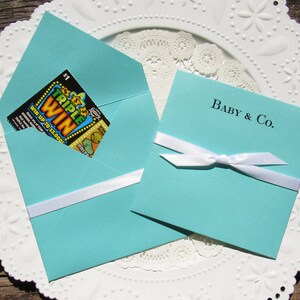 Tiffany Blue baby shower favors, personalized for the new baby.  Each is printed on tiffany blue card stock with a white ribbon tied around, slide a lottery ticket in for a fun and easy baby shower favor.