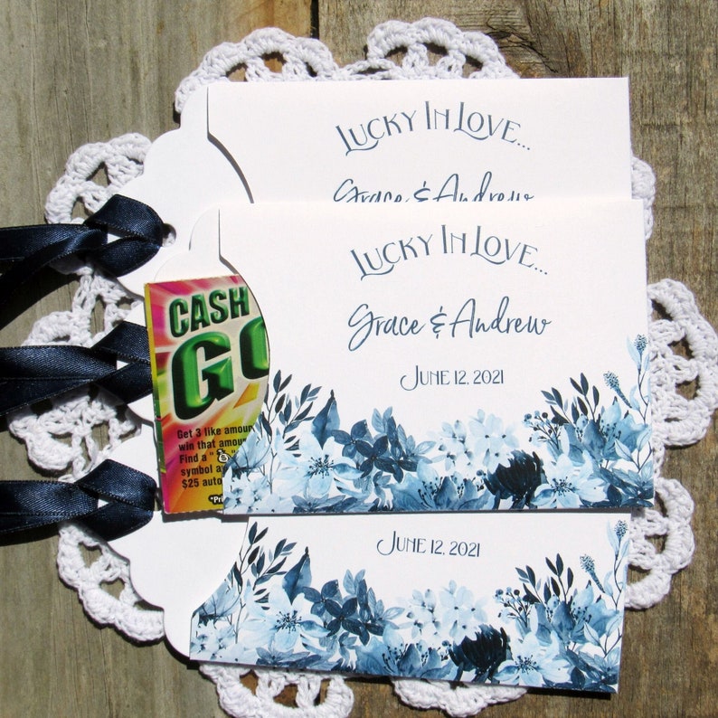 Blue wedding favors, personalized for the bride and groom.  White envelopes adorned with navy blue flowers and ribbon, printed with Lucky in Love.  Slide a scratch off ticket in to see who wins big.