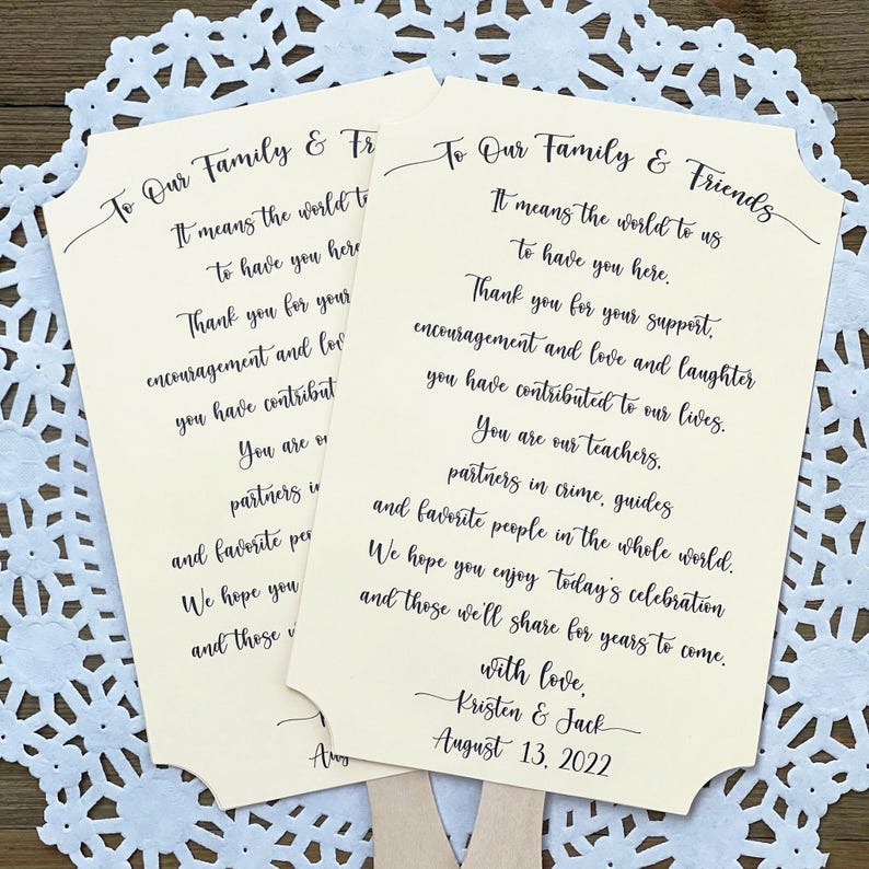May include: Two ivory wedding fans with black calligraphy text. The text reads "To Our Family & Friends" and includes a message of thanks to guests for their support and encouragement. The fans are decorated with a simple black border and the date "August 13, 2022".