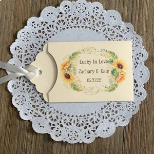 Puede incluir: Una tarjeta de regalo de boda de color crema con un dise&ntilde;o de girasol. La tarjeta dice "Lucky In Love Zachary & Kate 05.21.22".