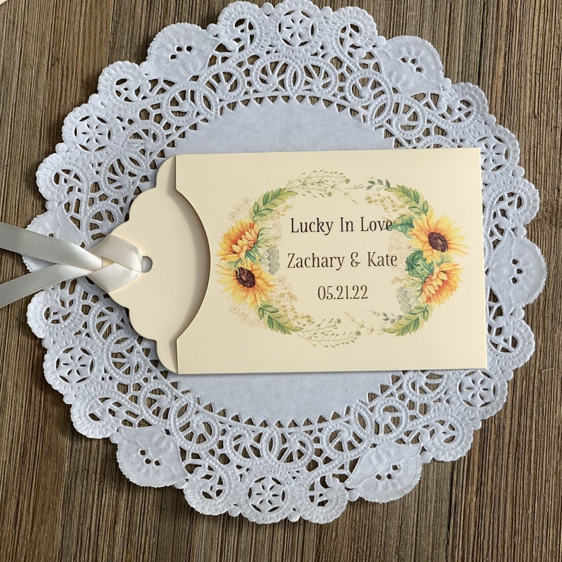 Puede incluir: Una tarjeta de regalo de boda de color crema con un dise&ntilde;o de girasol. La tarjeta dice "Lucky In Love Zachary & Kate 05.21.22".