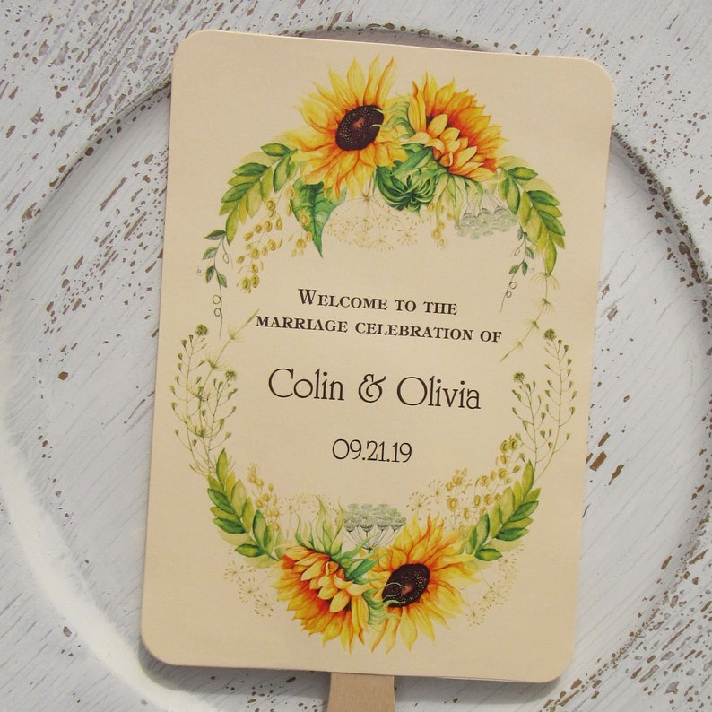 Sunflower wedding fans, personalized for the bride and groom adorned with a circle of sunflowers.  Printed on ivory cardstock with wooden handle hidden between front and back cardstock.  Wedding favor fans come fully assembled.