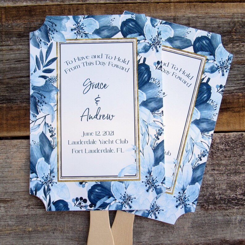 May include: Blue and white floral wedding fans with gold trim. The fans have the text "To Have and To Hold From This Day Forward Grace & Andrew June 12, 2021 Lauderdale Yacht Club Fort Lauderdale, FL" printed on them.