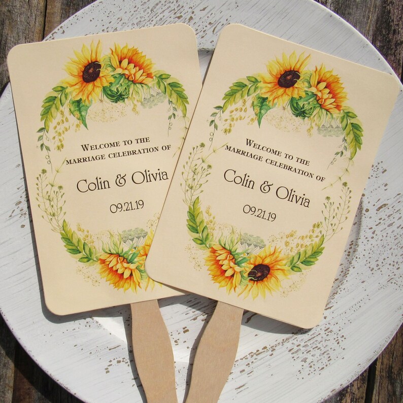 Sunflower wedding fans, personalized for the bride and groom adorned with a circle of sunflowers.  Printed on ivory cardstock with wooden handle hidden between front and back cardstock.  Wedding favor fans come fully assembled.