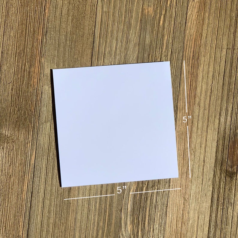 May include: A white, blank card measuring 5 inches by 5 inches. The card is lying flat on a wooden surface.