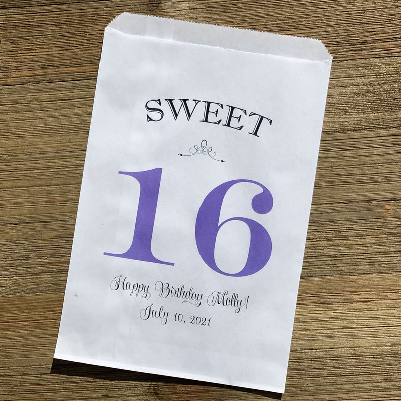 Op de afbeelding: Een witte papieren cadeauzak met de woorden "SWEET 16" in zwart en paars gedrukt. De zak bevat ook de tekst "Happy Birthday Molly! July 10, 2021" in een scriptlettertype. De zak ligt op een houten oppervlak.