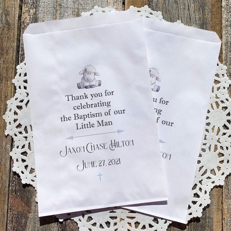 K&ouml;nnte beinhalten: Wei&szlig;e Papier-Geschenkbeutel mit einer blauen und grauen Lamm-Illustration. Die Beutel haben den Text "Vielen Dank f&uuml;r die Feier der Taufe unseres kleinen Mannes Jaxon Chase Hilton am 27. Juni 2021".