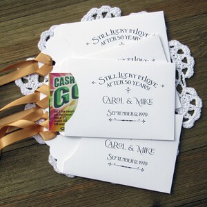 May include: Three white envelopes with gold ribbon ties. The envelopes have a pocket on the front and say "Still Lucky in Love After 50 Years!" with the names Carol & Mike and the date September 12, 1970.