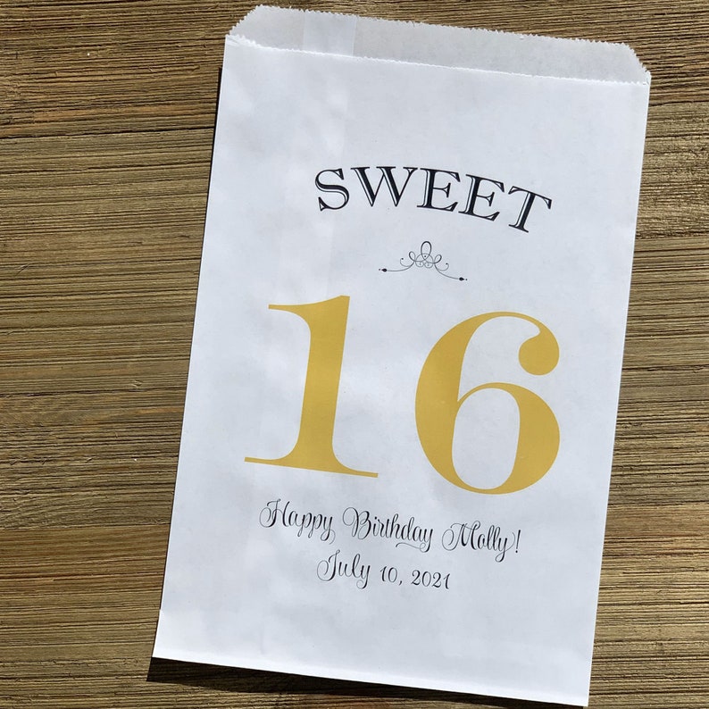 Op de afbeelding: Witte papieren traktatiezak met de woorden "SWEET 16" in zwarte en gouden letters. De zak bevat ook de tekst "Happy Birthday Molly! July 10, 2021". De zak is ontworpen voor een sweet sixteen verjaardag.
